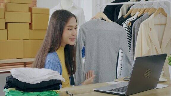 一位年轻的亚洲女性正在家里在线向顾客展示衣服中小企业