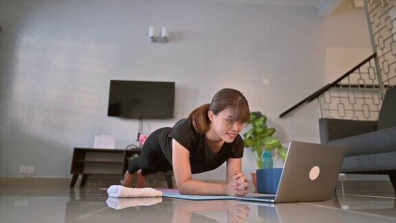 一位亚洲女性通过笔记本电脑上的直播视频进行瑜伽练习