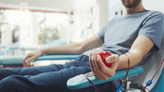 男性献血者的手的特写镜头白人男子挤压心形红球将血液通过管道泵入袋中捐赠给心脏手术患者