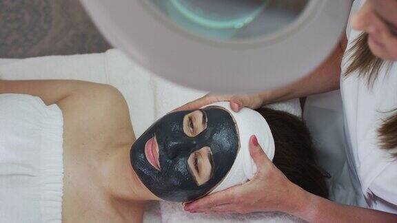 白种妇女躺下来而美容师给她一个面具