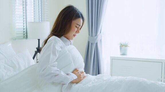 亚洲美丽生病的女孩在睡衣起床在卧室有魅力的年轻女性在床上醒来后会感觉很难受肚子疼或者早上抱肚子