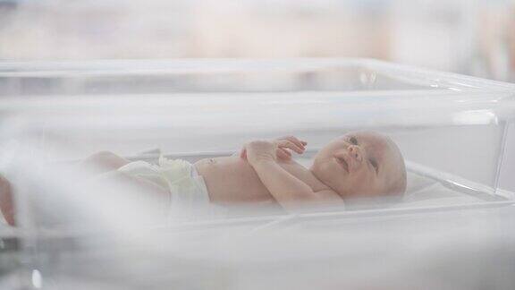 可爱的小白种人新生儿躺在妇产科医院保温箱的摇篮里一个顽皮而充满活力的小孩子的肖像保健、怀孕和母亲概念