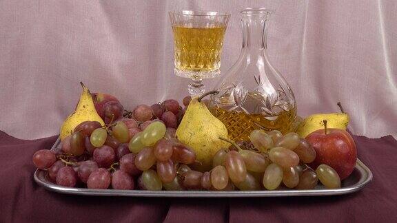 一个水晶醒酒器一杯葡萄酒和一个托盘上的各种水果是粉红色和酒红色的纺织品背景