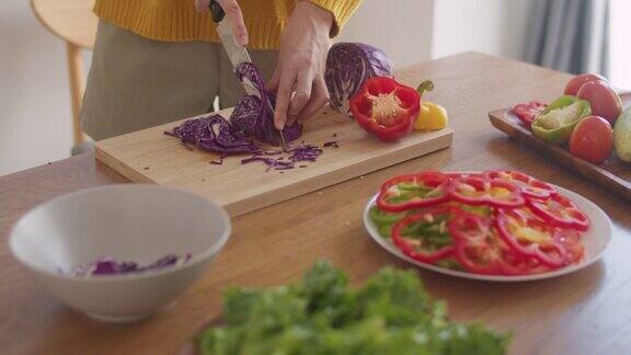 一个亚洲妇女在家里的厨房里在一块木板上切红卷心菜蔬菜准备食物做沙拉的特写部分