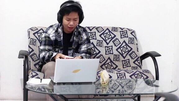 亚洲男性工作在家里使用笔记本电脑视频会议电话会议耳机