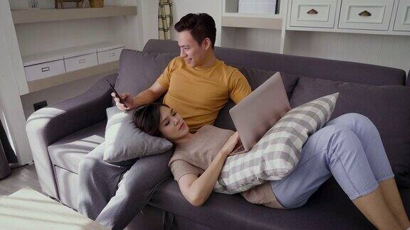 年轻的亚洲幸福夫妇使用笔记本电脑和手机在客厅夫妇放松和花时间在一起在家里