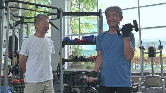 亚裔华人高级私人教练鼓励年长男子在健身房练习哑铃