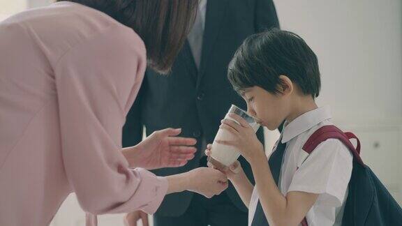 放学后欢迎回家美丽的亚洲妈妈正等着她的小儿子从学校回来手里拿着一杯牛奶小学生小男孩放学后正在喝鲜奶