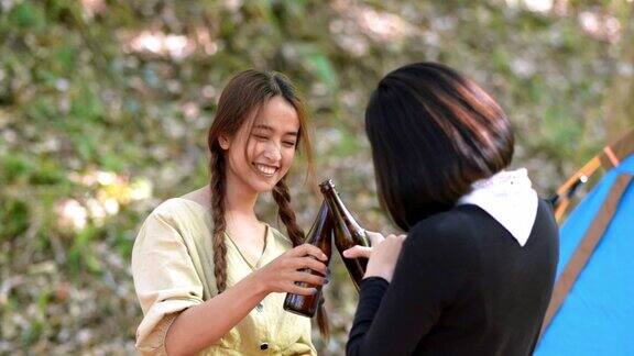 年轻女子在露营帐篷前跳舞和喝饮料