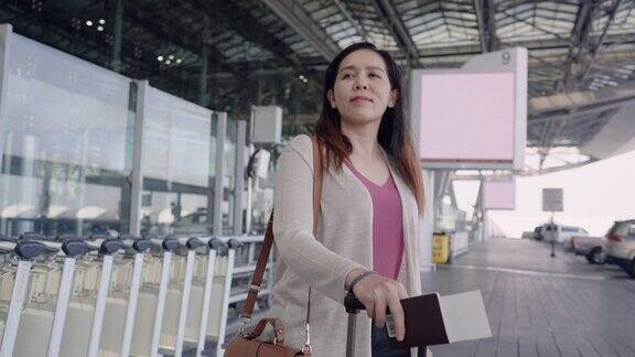 一名亚洲女性旅客在机场拿着行李、护照和机票在出租车等候站等着她的朋友一起旅行然后登机