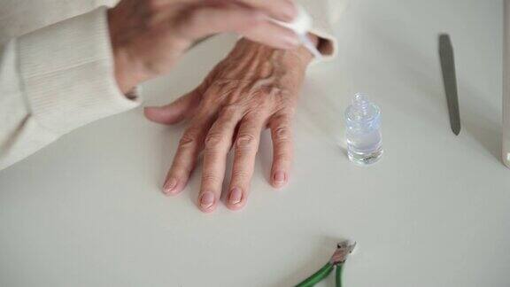有皱纹的老妇人在指甲上涂透明指甲油