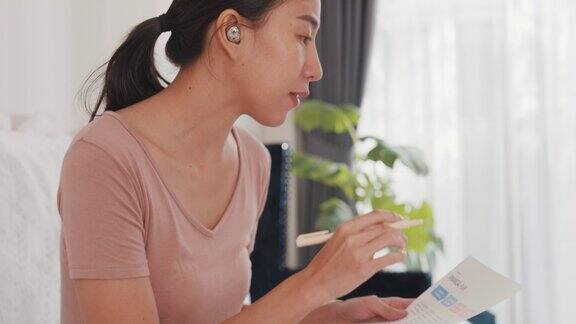 年轻的亚洲女商人使用笔记本电脑在视频电话会议上与同事谈论计划而在家中的客厅工作