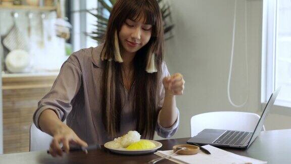 亚洲妇女吃芒果糯米饭同时在桌子上工作