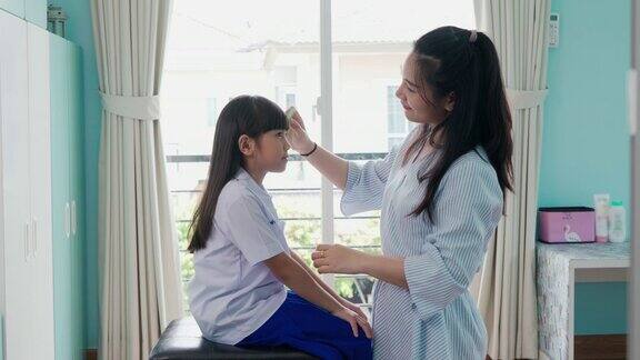 亚洲母亲梳理她的女儿的头发在早上上学前在家里的客厅早上学校的日常生活为上学做准备