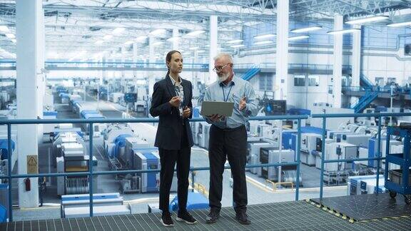男工程师和女工程师站在工厂里使用笔记本电脑在工厂里与为不同行业生产现代电子元件的设备交谈