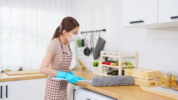 亚洲清洁服务女工在家里的厨房打扫漂亮女孩管家戴上清洁口罩并用鸡毛掸子擦拭凌乱的柜台进行家务或杂务的家务整理