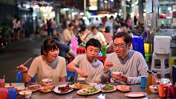 4K亚洲家庭在曼谷Yaowarat路的街头美食餐厅和人群一起享用美食