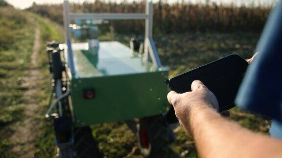 面目全非的男人驾驶着农业机器人通过田地用平板电脑控制它