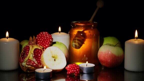 蜂蜜新鲜苹果和石榴黑色背景上燃烧的蜡烛