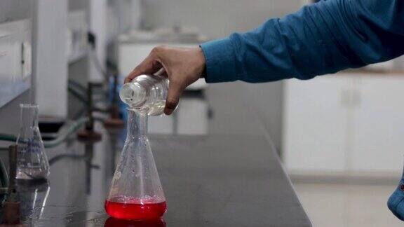 一个研究科学家的手从一个瓶子倒入一个红色的化学物质在一个锥形烧瓶