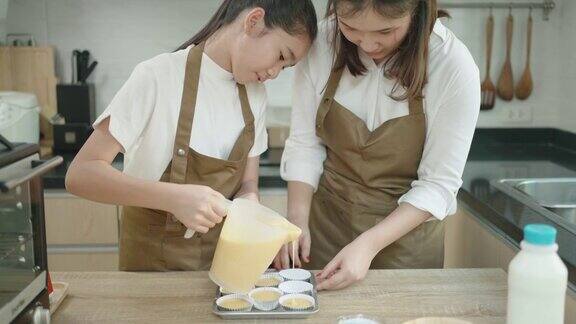 一名亚洲少女正在通过智能手机与老师在线学习做面包她的母亲帮助设置厨房的设备在家里