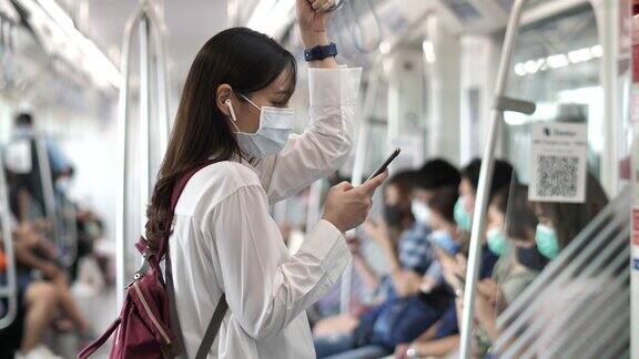 亚洲女性戴着口罩在地铁上使用智能手机