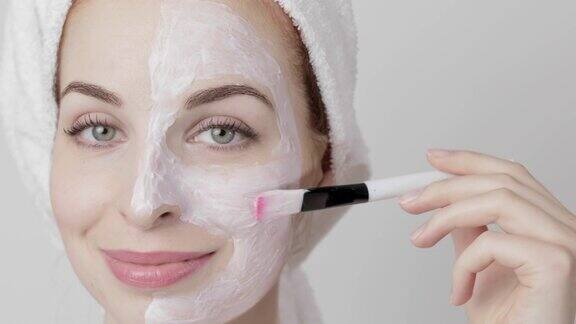 女士用毛巾在头上敷面膜在脸上使用化妆刷在灰色背景