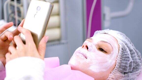 一名女子戴着面具躺在美容师的办公室里看手机里的东西
