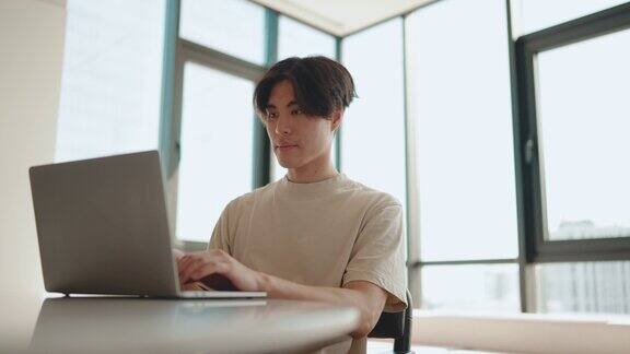 自信的年轻亚洲男子在厨房用笔记本电脑工作
