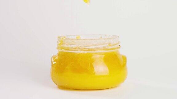 蜂蜜和蜂蜡从罐子里的蜂蜜勺滴下来背景是白色的天然蜂蜜液体从滴管流下