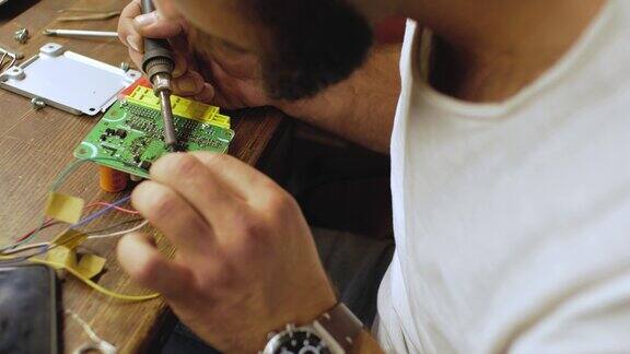 一个留着胡子的电工正在焊接一个微电路这家伙是用烙铁工作的修理电气设备从以上观点4k的视频