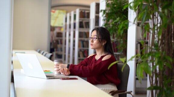 年轻的亚洲学生女孩在大学图书馆学习与笔记本电脑准备考试做研究