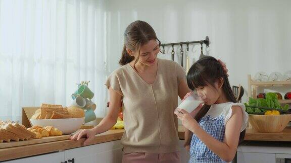 亚洲小可爱的孩子拿着一杯牛奶和喝妈妈迷人的妈妈教导和支持年轻的女儿照顾她的身体喝牛奶后醒来在家里的保健