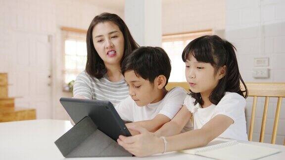 快乐亚洲家庭家庭教育母亲教孩子在家里的客厅使用数码平板电脑