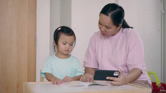 一位亚洲母亲在家用智能手机照顾女儿在线学习