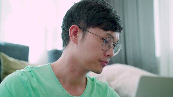 4K一个年轻的亚洲人的特写穿着绿色衬衫在他的工作上严肃的表情在房子里