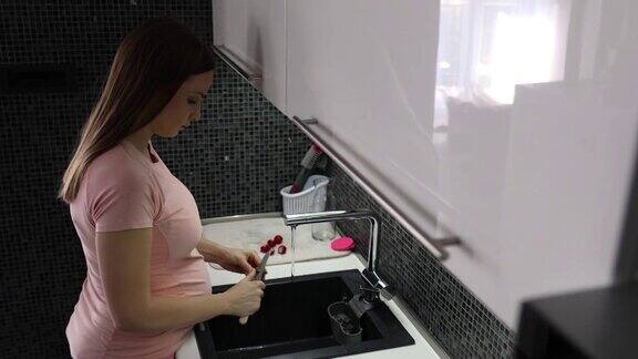 美丽的孕妇站在厨房水槽边为沙拉清洗新鲜的有机蔬菜