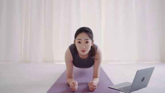 年轻的亚洲女性看着笔记本电脑在室内练习瑜伽