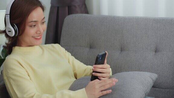 亚洲女性放松地坐在家里的沙发上拿着手机听音乐