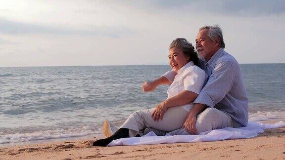 年长的亚洲夫妇坐在海滩上看着日落一起快乐的情绪有生活方式、情感和退休观念的人