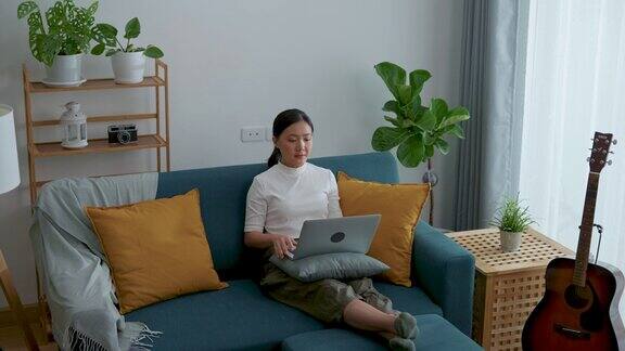亚洲女性坐在家里的客厅里用笔记本电脑进行视频通话