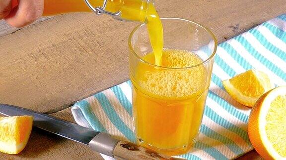 倒橙汁在玻璃与切片水果在木质背景和织物