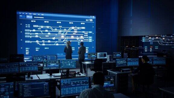 项目经理和计算机科学工程师在使用大屏幕显示基础设施信息图和数据时交谈电信公司系统控制和监控室