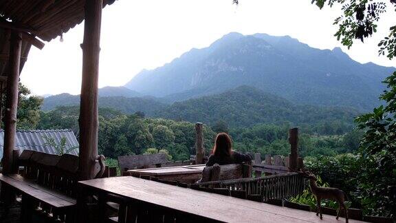 一位女游客坐在木制阳台上看着美丽的山景