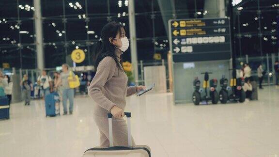 亚洲女乘客戴着外科口罩提着行李箱在机场候机楼行走