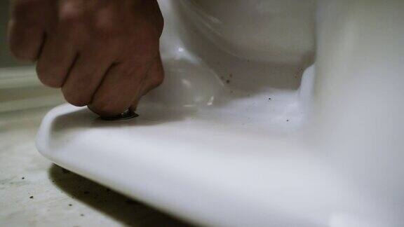 一个白人修理工把一个螺母放到一个法兰螺栓上然后用手指把它拧紧把一个瓷马桶固定在一个室内家用浴室的地板上