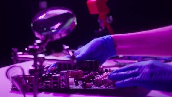 在霓虹灯中组装主板的特写在蓝色防护手套中固定小玩意的细节在电子设备工厂用放大镜和螺丝刀修理电脑零件