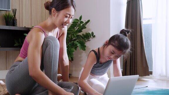 迷人的亚洲女性和女孩练习瑜伽在线课程与笔记本电脑在家里