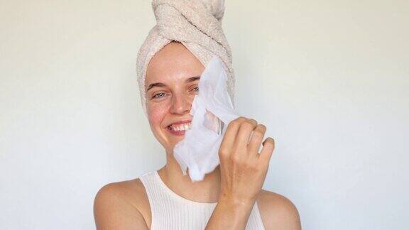 日常自我护理程序快乐的年轻女性从面部护肤品中去除含有胶原质透明质酸的保湿面膜使用保湿面膜发光皮肤