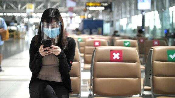 亚洲女性在机场使用智能手机时戴上口罩新常态概念